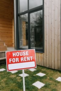 House for rent sign standing on the grassy front lawn of a single-family home being offered as a rental